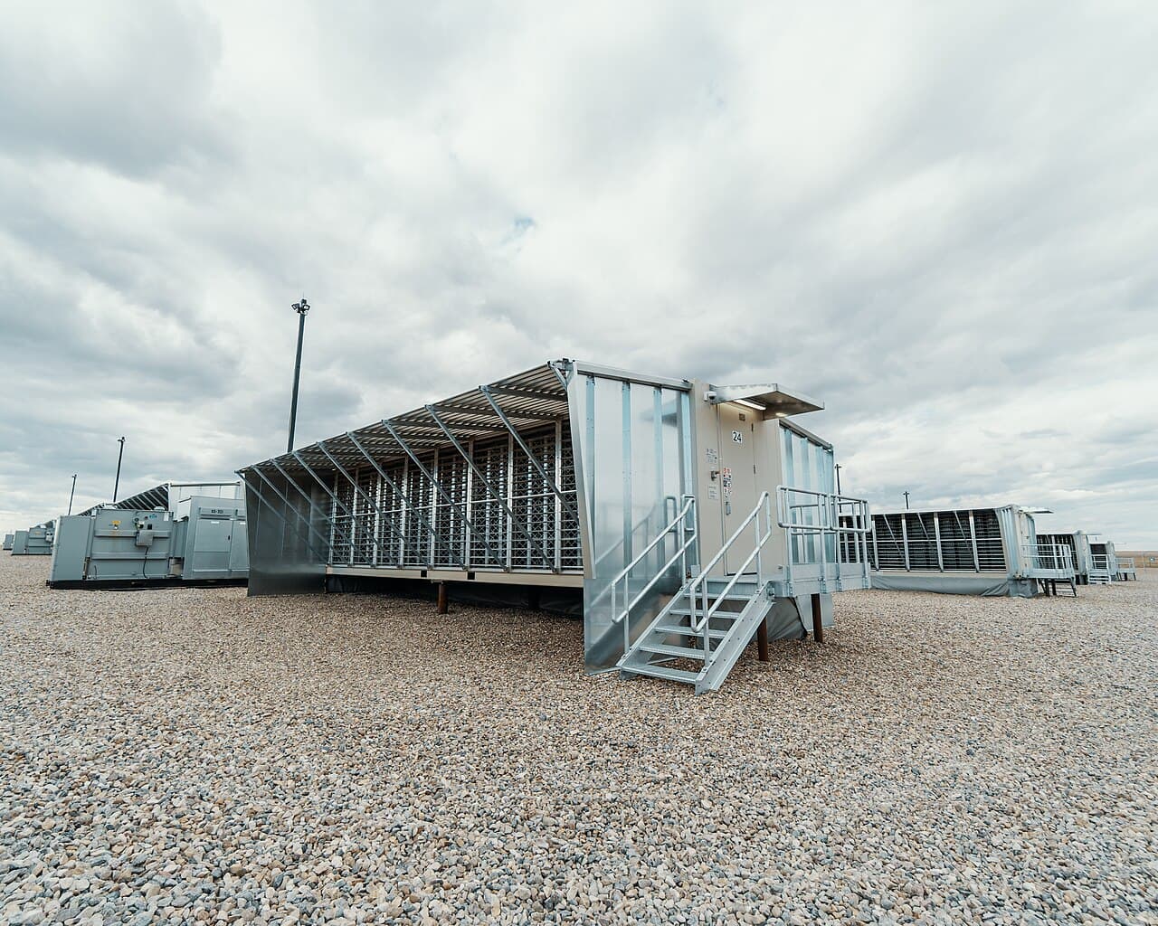 A containerised mining unit with louvred sides and an access stair, on a gravel site