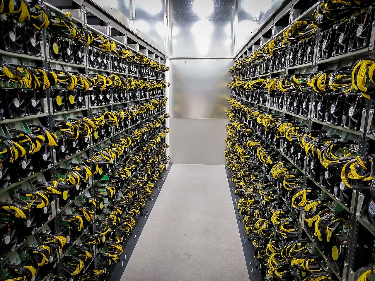 An aisle between two walls of racked air-cooled miners with yellow power cables